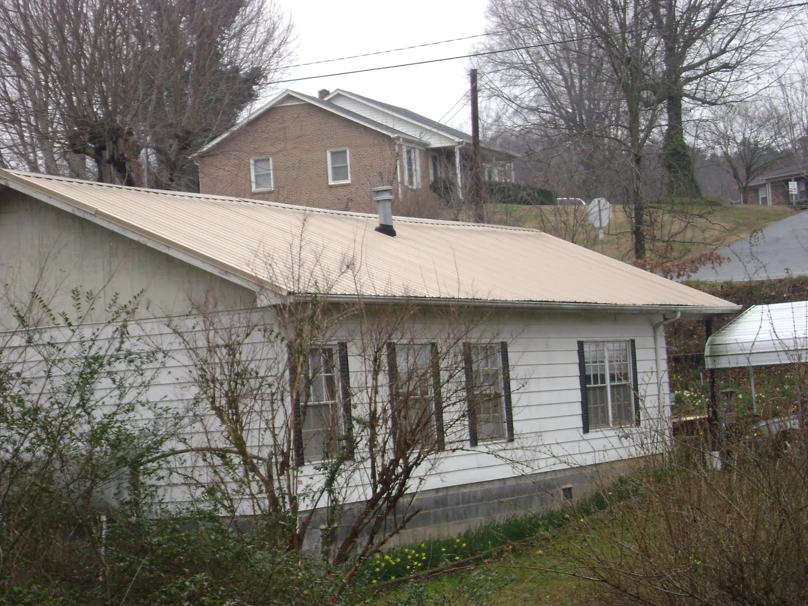 Tan metal roof on a white sided house set into a hillside — Commercial Roofing by Roofing Brothers in Granby